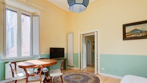 A room with a dining table, chairs, a television, a patterned rug, and a painting on the wall. - Babuino by Interhome (Roma: Piazza di Spagna)