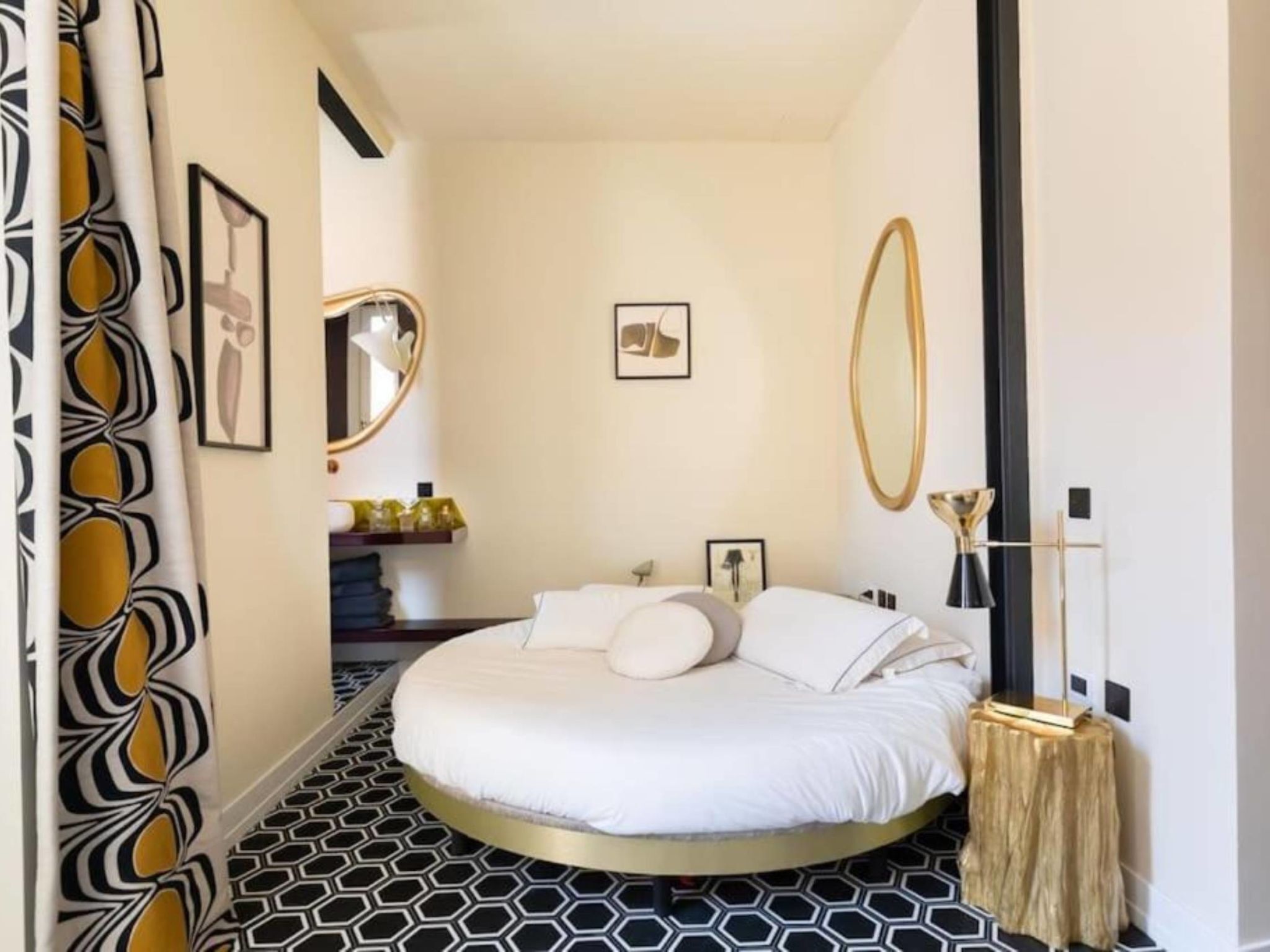 A modern bedroom with a round bed, a mirror, and a geometric patterned floor.