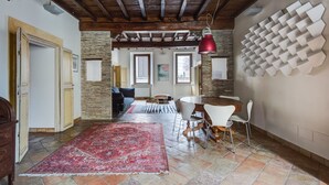 A spacious room with a red carpet, stone walls, a wooden ceiling, and a dining area with white chairs and a red pendant light. - Pantheon View by Interhome (Roma: Piazza Navona - Campo dei Fiori)