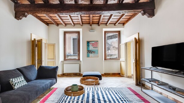 A living room with a dark sofa, a striped rug, a television on a stand, and a wooden ceiling. - Pantheon View by Interhome (Roma: Piazza Navona - Campo dei Fiori)
