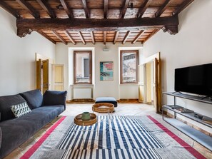 A living room with a dark sofa, a striped rug, a television on a stand, and a wooden ceiling. - Pantheon View by Interhome (Roma: Piazza Navona - Campo dei Fiori)