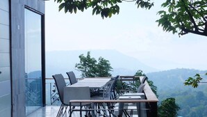 Een moderne buiten eethoek met glazen balustrade, een tafel en stoelen, met uitzicht op een bergachtig landschap.