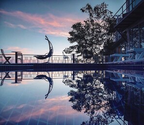 A serene outdoor pool area with modern seating and a clear reflection of the sky and surrounding trees. - The Resort Angel Hill (Pak Chong)