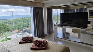 Een hotelkamer met een groot bed, een televisie en een balkon met uitzicht op het landschap.