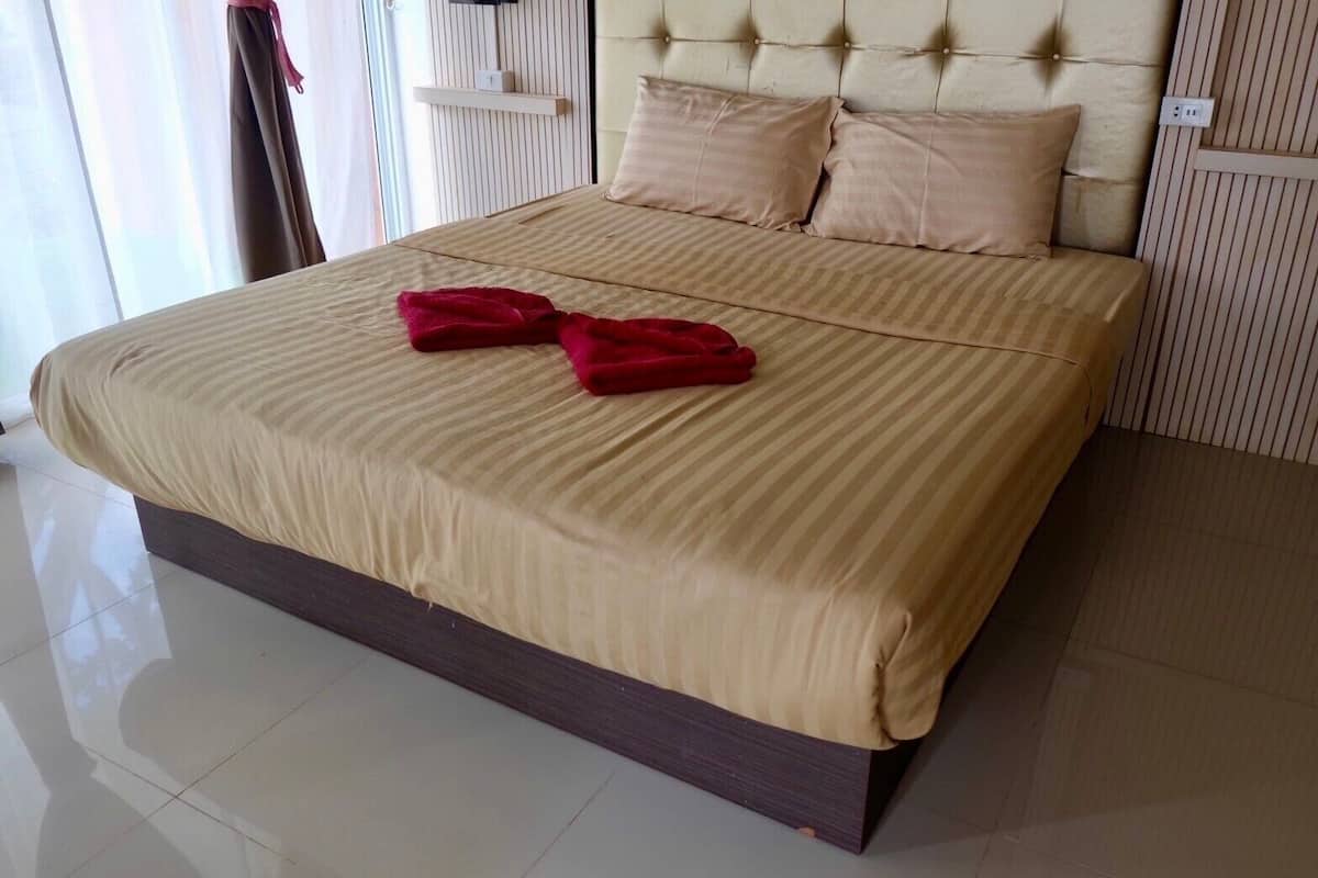 A large bed with a striped beige bedspread and two red towels, a tufted headboard, and a wooden shelf above the bed.