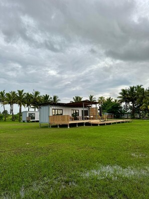A modern, single-story structure with a deck and outdoor seating area, surrounded by palm trees and grassy fields. - Selah Fiji (Nadi)