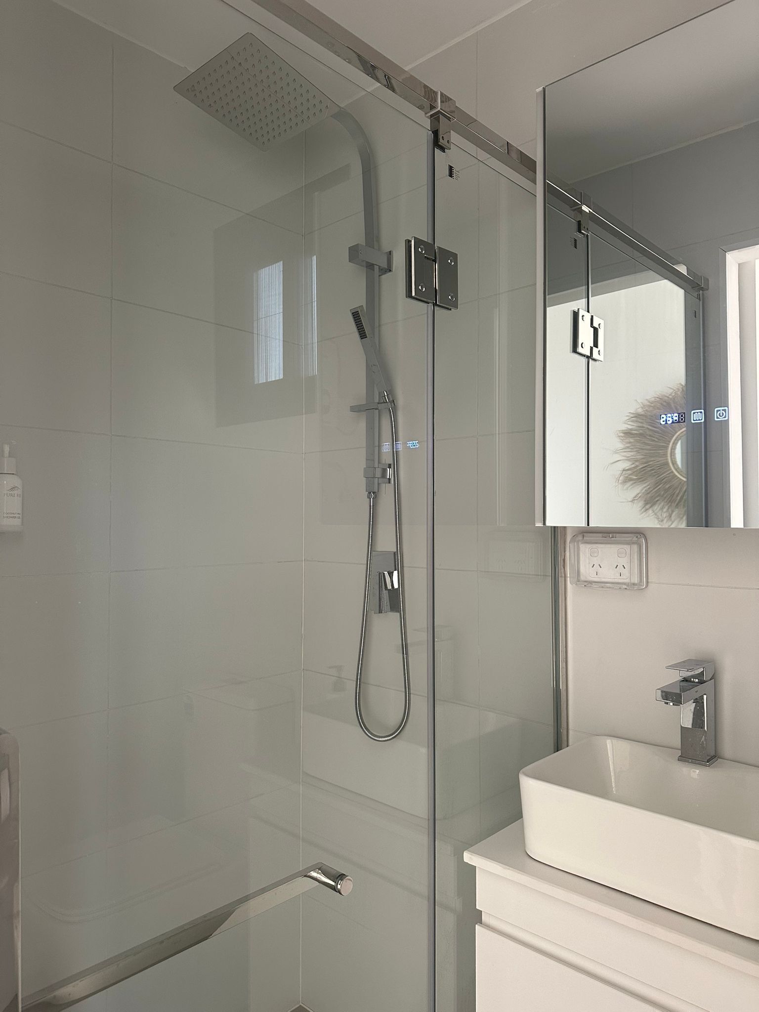 Ein modernes Badezimmer mit einer gläsernen Duschkabine, einem weißen Waschbecken und einem Spiegel darüber.