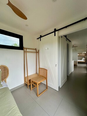 A minimalist bedroom with a bed, a wooden chair, a ladder, and a sliding door. - Selah Fiji (Nadi)