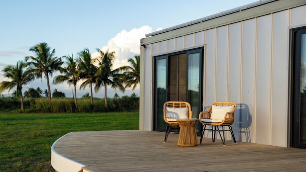 A deck with two wicker chairs and a small table, overlooking a grassy area with palm trees. - Selah Fiji (Nadi)