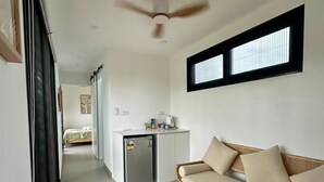 A modern, well-lit room with a ceiling fan, a sofa, a small table, and a kitchenette area. - Selah Fiji (Nadi)