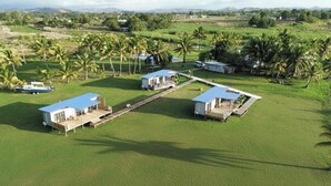 A large, open grassy area with several small, modern buildings, likely guest houses or cottages, arranged in a semi-circle. - Selah Fiji (Nadi)