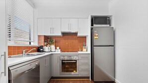 A compact kitchen with white cabinets, a built-in oven, a microwave, and a dishwasher. - Balaclava City Hub by Ready Set Stay (Balaclava)