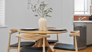 A dining area with a round wooden table, black cushioned chairs, a white vase with a plant, and a small candle. - Balaclava City Hub by Ready Set Stay (Balaclava)