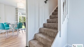 A staircase with carpeted steps and a handrail, leading to a room with a dining area featuring teal chairs and a table with wine glasses. - Lime Corner: Peaceful with Parking (Leicester)