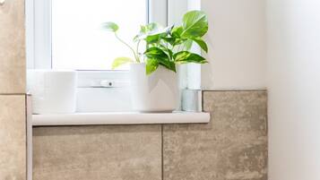Une salle de bain avec une fenêtre, un lavabo blanc et une plante en pot.
