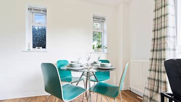 A dining area with a round table, teal chairs, and a window with a view of trees.