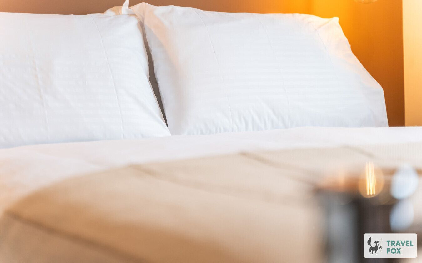 Un lit avec une literie blanche et un logo représentant un renard, symbole de la marque de voyage, visible sur le mur.