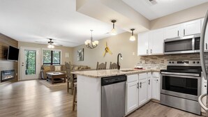 A modern kitchen with white cabinets, stainless steel appliances, and a central island with a dishwasher. - Lavish Waterfront Condo 60ft from Table Rock Lake! (Branson)