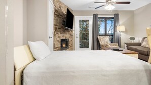 A hotel room with a large bed, a fireplace, a ceiling fan, a TV mounted on the wall, and a view of the outdoors through a glass door. - Lakefront Condo, 2 min to Silver Dollar City! Ticket Deals & Resort Perks (Branson)