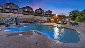 A pool area with a slide, lounge chairs, and a building with multiple balconies. - Lakefront Condo, 2 min to Silver Dollar City! Ticket Deals & Resort Perks (Branson)