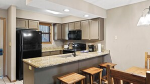 A kitchen with a black refrigerator, a microwave, a coffee maker, and wooden stools.