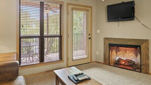 A living room with a fireplace, a television mounted on the wall, and a table with a remote control.
