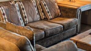A leather sofa with patterned cushions, a wooden side table with a lamp, and a framed picture on the wall.