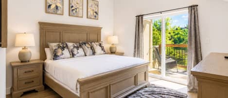 A bedroom with a large bed, two bedside tables, a nightstand, a window with curtains, and a view of greenery outside.