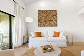 Ein modernes Wohnzimmer mit einem weißen Sofa, einem runden Couchtisch und einem großen Wandteppich.