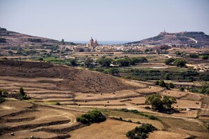 Un paysage rural caractérisé par des champs en terrasses, une église imposante et une forteresse située au sommet d’une colline.