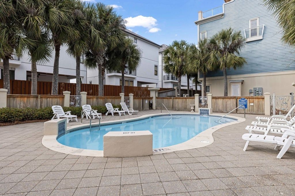 A swimming pool with lounge chairs, palm trees, and a wooden fence.