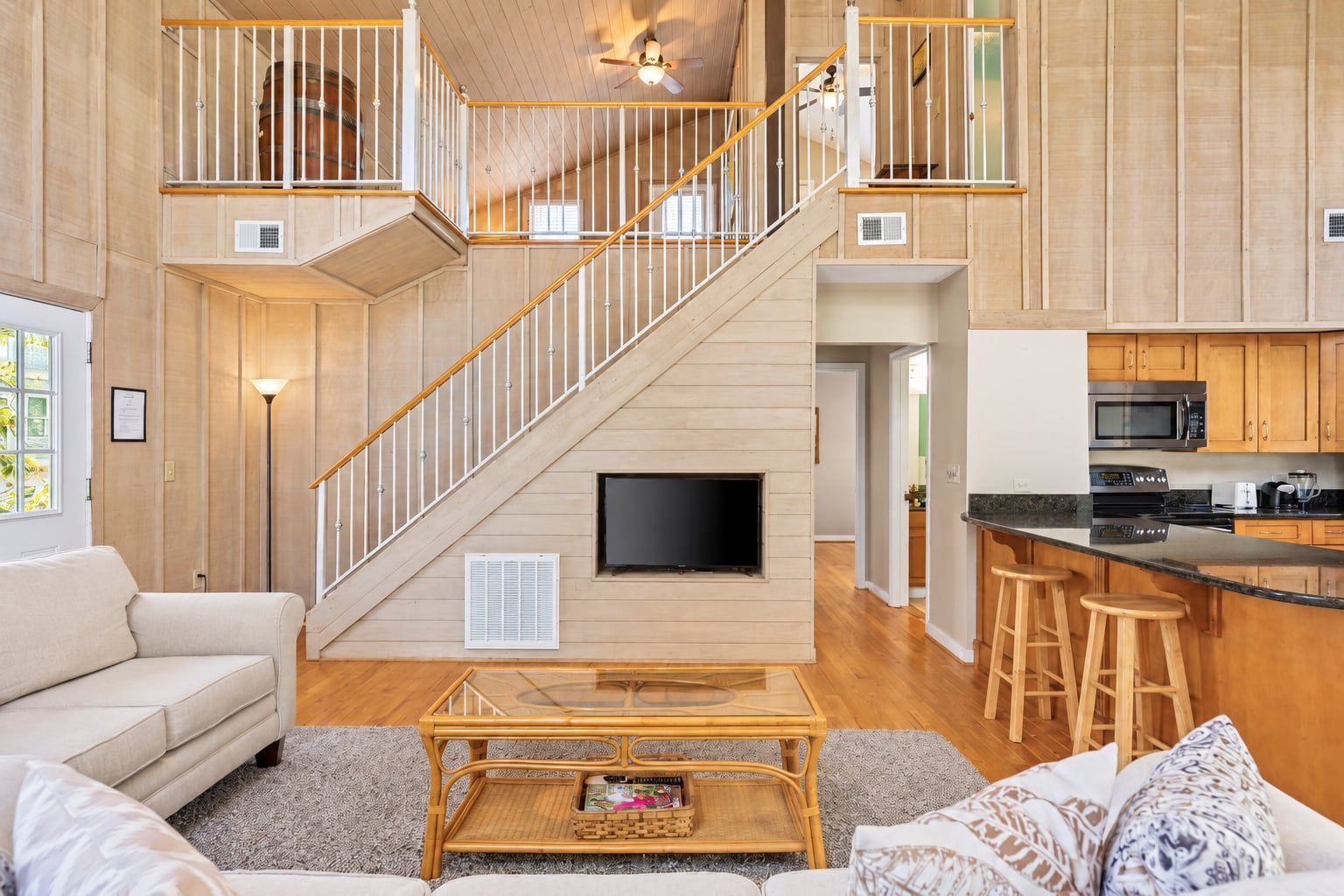 Un vaste espace de vie agrémenté d’un escalier en bois, d’un téléviseur à écran plat, d’une cuisine équipée d’appareils modernes et d’un coin bar avec des tabourets.