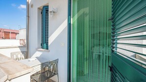 Ein Balkon mit Tisch und Stühlen, eine grüne Tür und ein Fenster mit Jalousien.