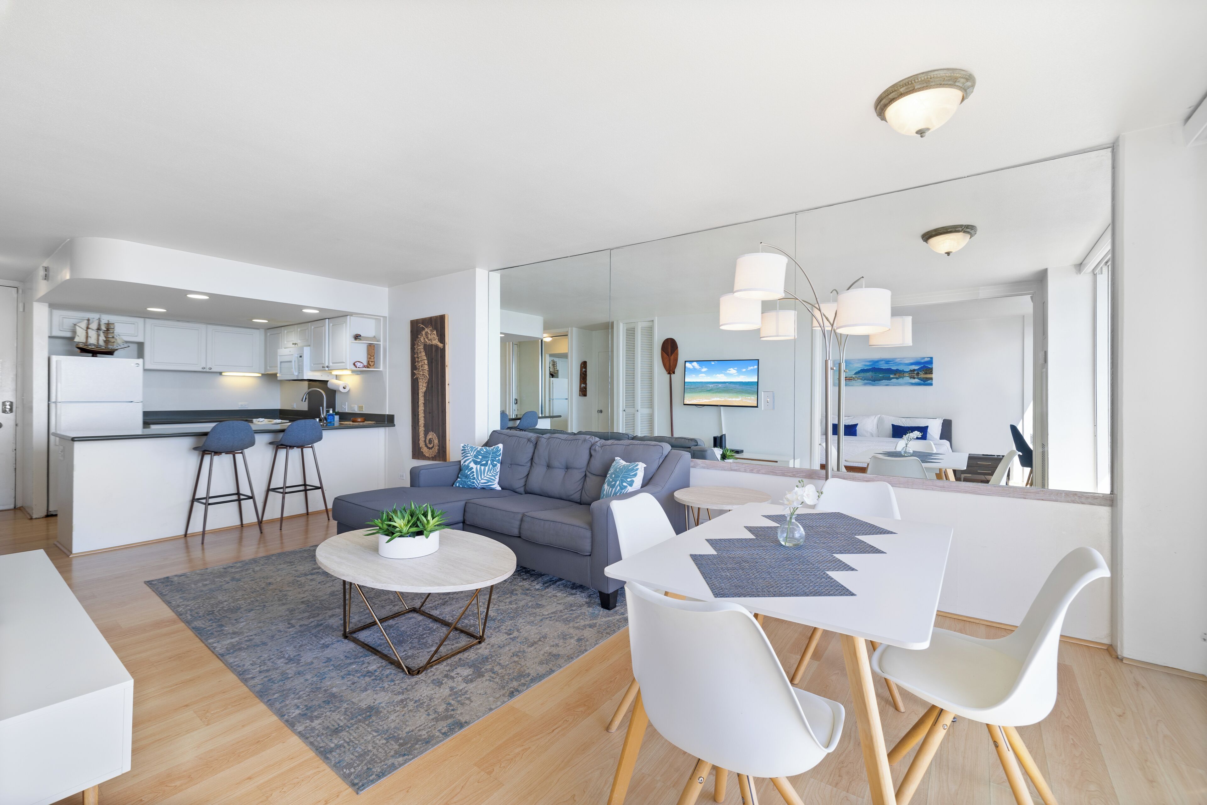 A modern living room with a grey sofa, a round coffee table, and a dining area with a white table and chairs.