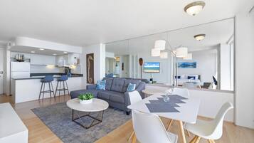 A modern living room with a grey sofa, a round coffee table, and a dining area with a white table and chairs.