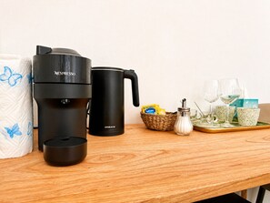 A coffee maker, a mug, a basket with snacks, and glasses on a wooden table. - Vertigini Suites (Riomaggiore)
