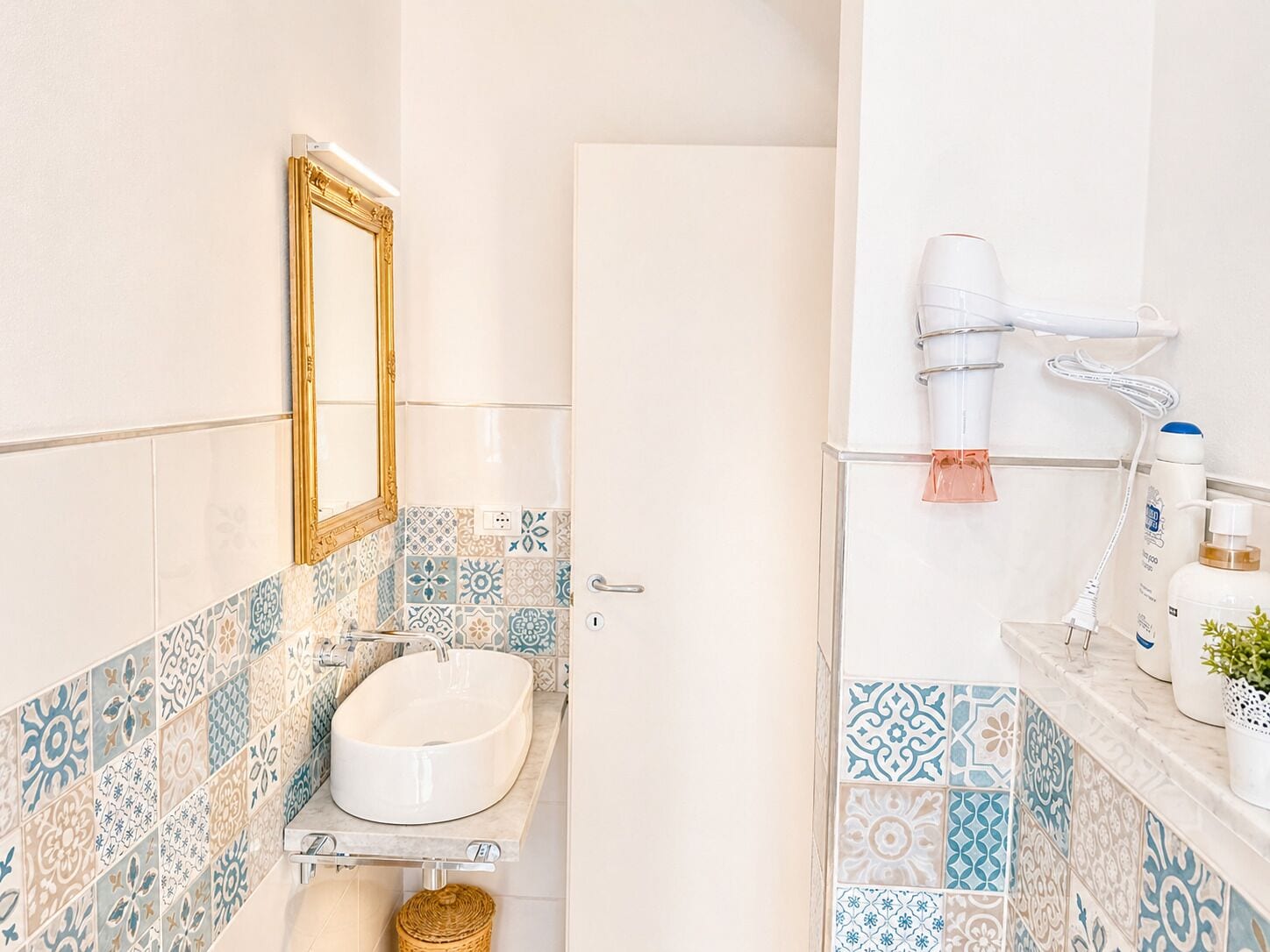 A bathroom with a white sink, a mirror with a gold frame, and a towel rack with a pink towel.