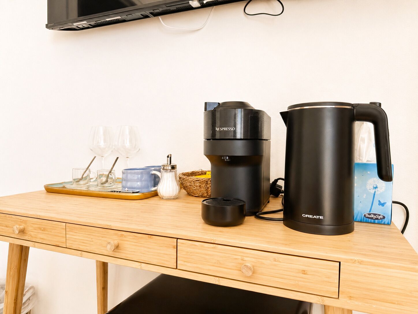A wooden table with a coffee maker, a kettle, glasses, and a basket.