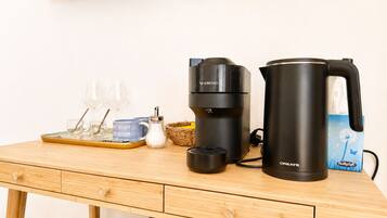 A wooden table with a coffee maker, a kettle, glasses, and a basket.
