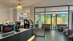Un café moderno con una máquina de café, zona de estar y amplios ventanales que ofrecen vistas al exterior.