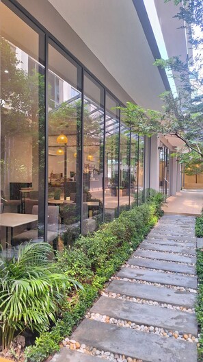 A modern outdoor seating area with glass walls, stone pathway, and greenery. - 35 Bow Hotel (Bangkok)