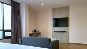 Ein Hotelzimmer mit einem großen Bett, einem Schreibtisch mit Stuhl, einem flachbildfernseher an der Wand und einem fenster mit Vorhängen.
