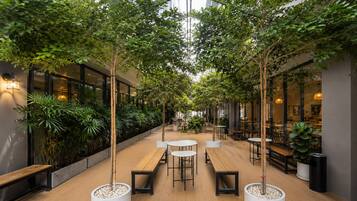 Un atrio interior con suelo de madera, mesas, bancos y plantas en macetas.