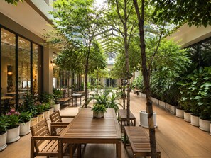 An indoor garden with wooden tables and chairs, surrounded by potted plants and trees. - 35 Bow Hotel (Bangkok)