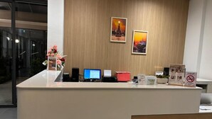 A reception desk with a wooden panel wall, two framed pictures, a computer, a red box, a tip box, and a no-smoking sign. - 35 Bow Hotel (Bangkok)