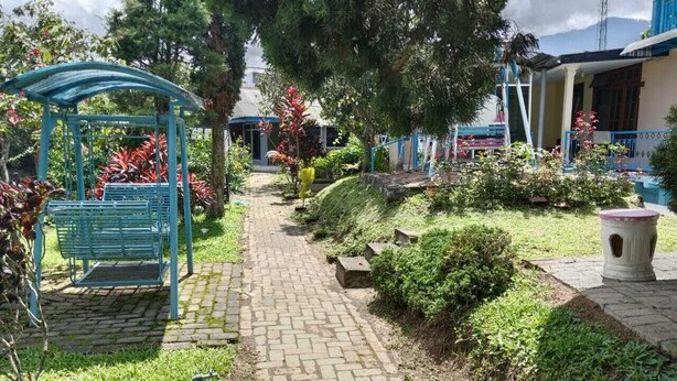 Ein gepflasterter Weg führt durch einen Garten mit einem blauen Kiosk und Bänken.