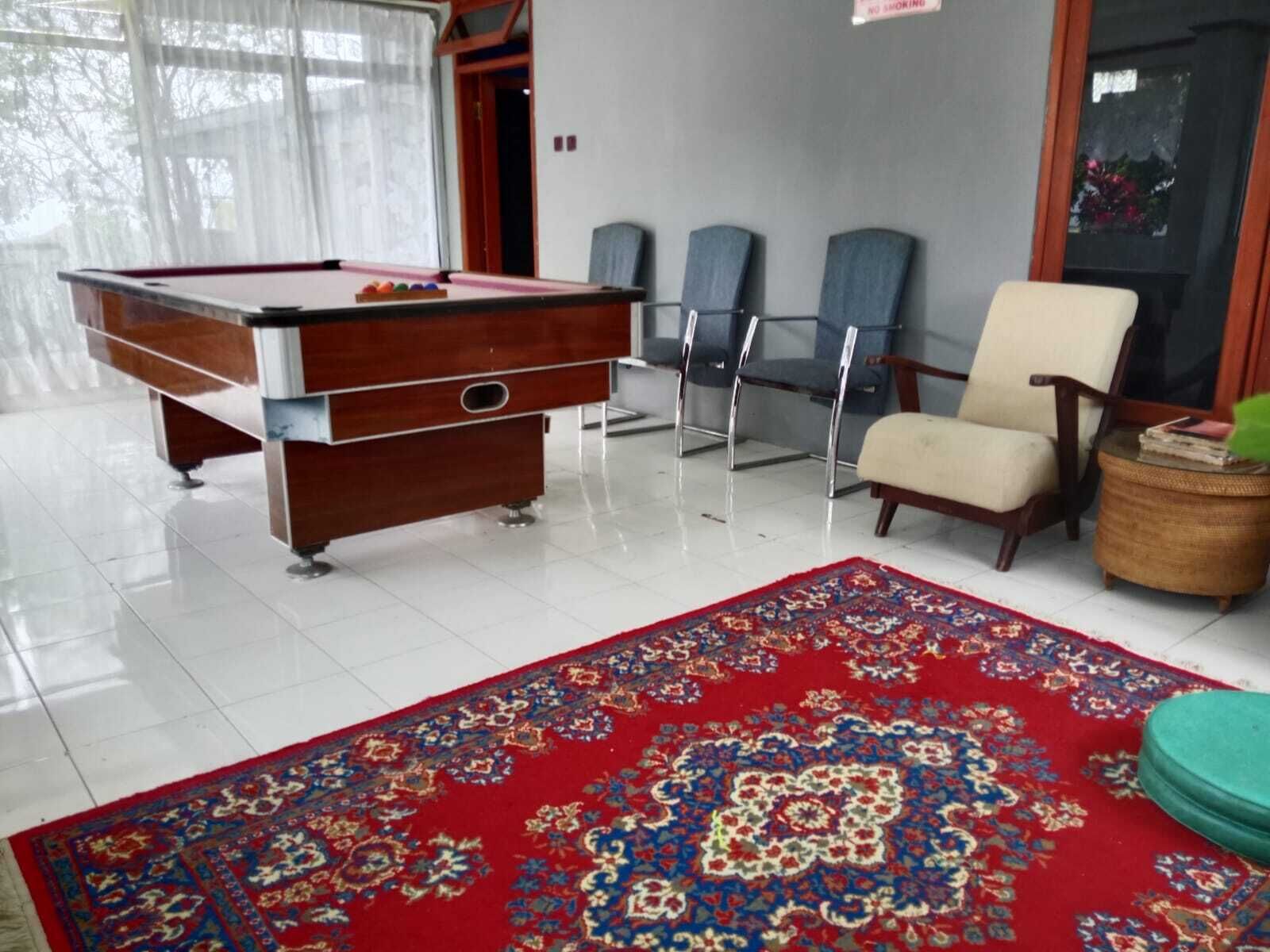 A billiards table, a red patterned carpet, and a chair in a room with a tiled floor.