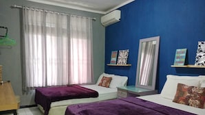 Ein Hotelzimmer mit zwei Betten, einem Schreibtisch, einem Stuhl, einem Fenster mit transparenten Vorhängen und Wanddekorationen.