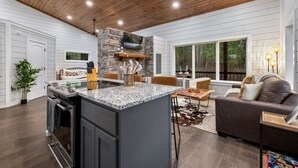 A modern kitchen with a granite island, wooden ceiling, and a stone accent wall. - Over the Moon · Sauna & Hot Tub at Modern Intimate Escape (Broken Bow)