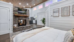 A bedroom with a large bed, a fireplace, a kitchen area, and a view of the outdoors. - Over the Moon · Sauna & Hot Tub at Modern Intimate Escape (Broken Bow)